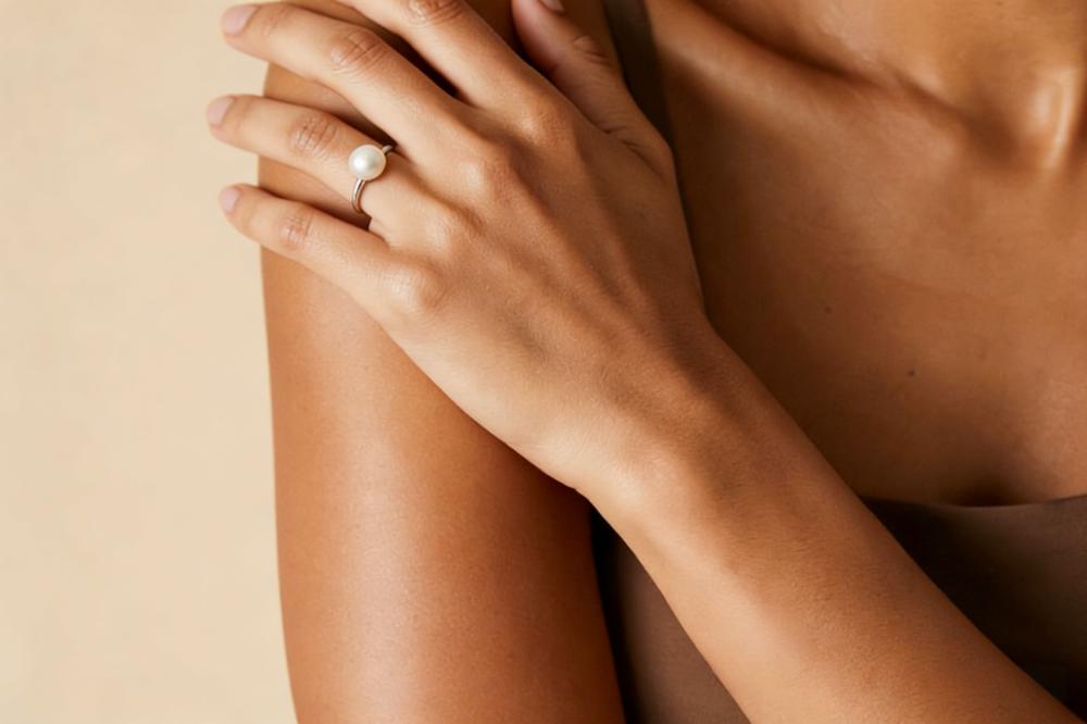 Close-up shot of a model's hand wearing a delicate pearl ring, with fingers relaxed and posed naturally as if gently resting on a surface.